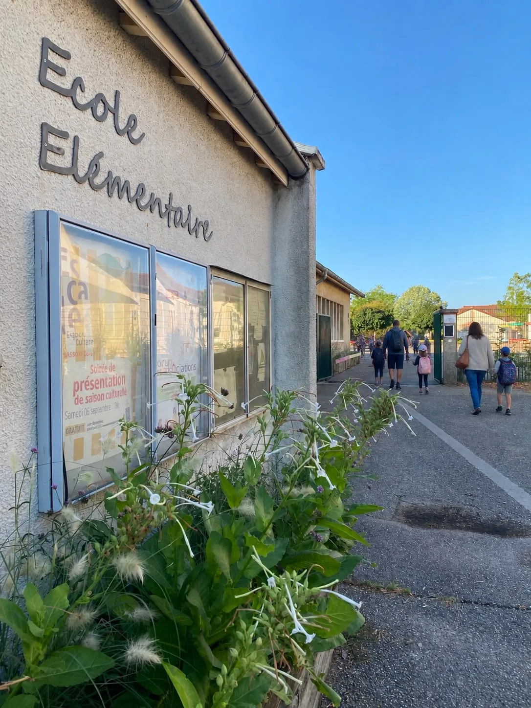 L’entrée de l’école élémentaire Victor Hugo un matin, avec des parents et des enfants de dos dans l’allée